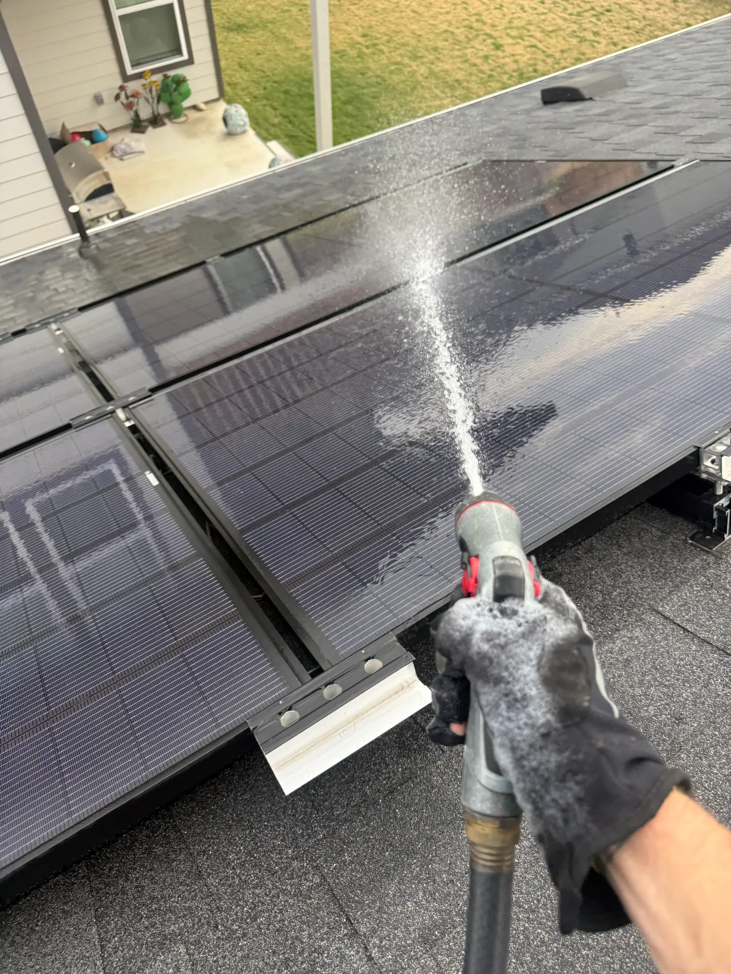 Gloved hand rinsing solar panels with a filtered spray nozzle