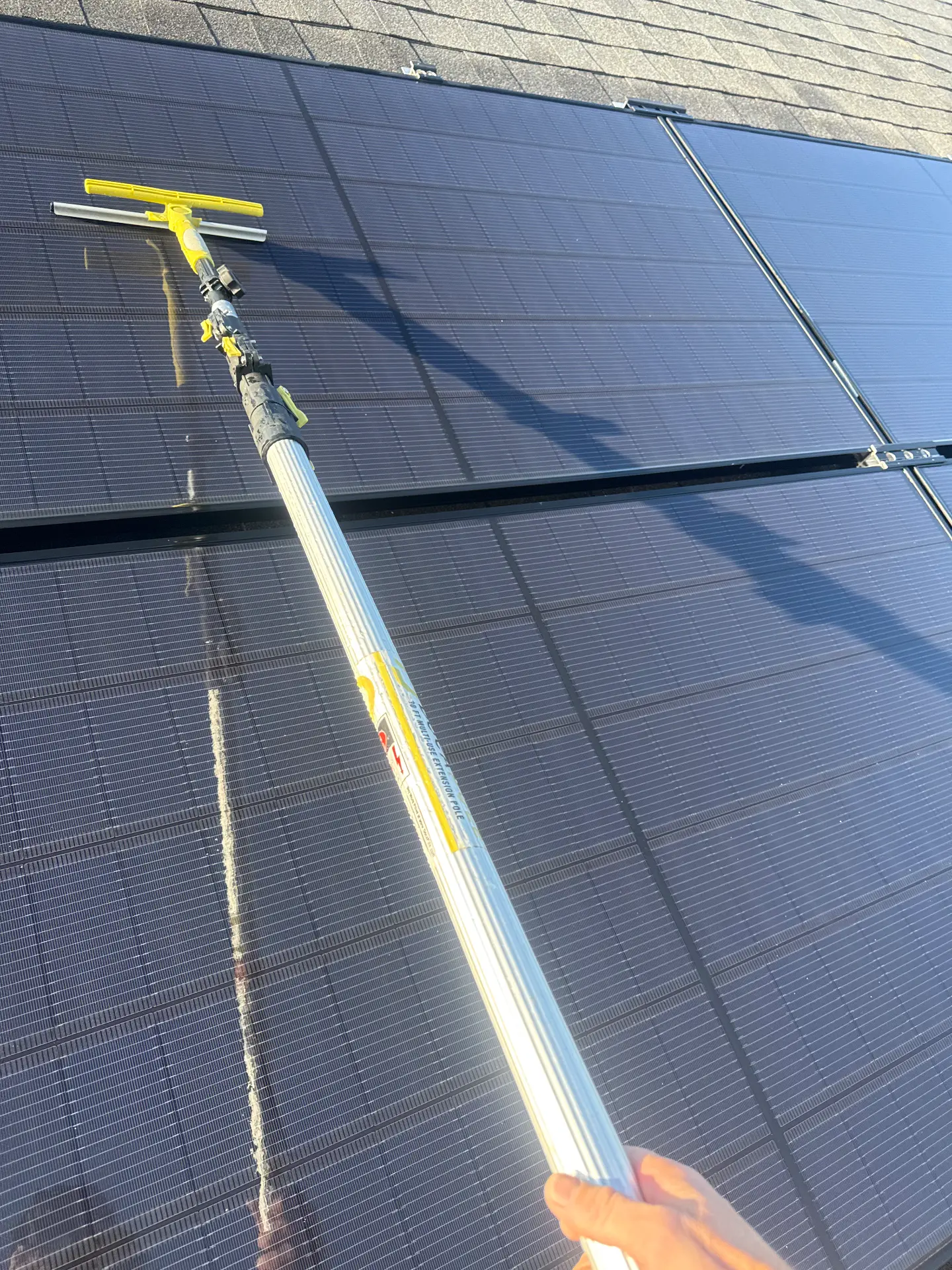 Squeegee pulling clean water off a solar panel on a Kyle roof